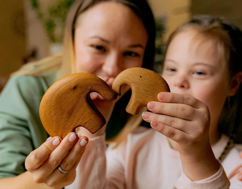 A woman and a young girl joyfully fitting wooden puzzle pieces together, using play as therapy according to her occupational therapy module1