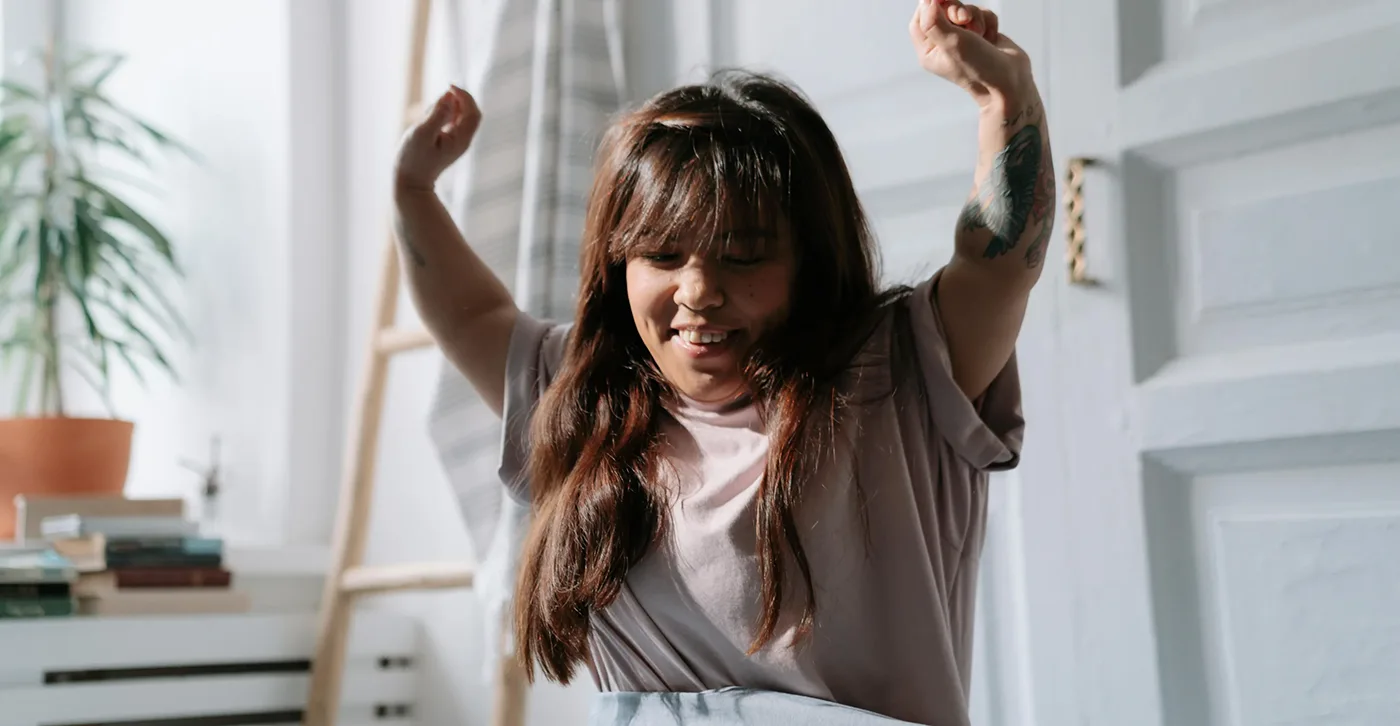 A woman with dwarfism stretching and smiling while sitting in a bright, cozy room. copy