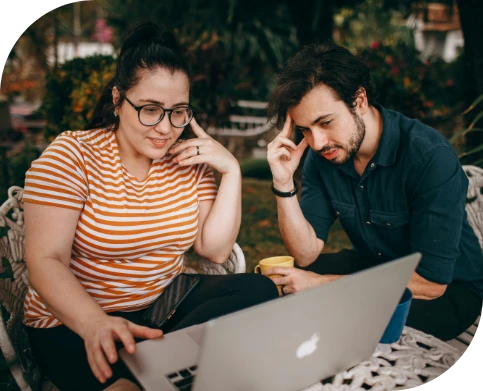 A man and woman focused on a laptop, engaged in a collaborative discussion outdoors.