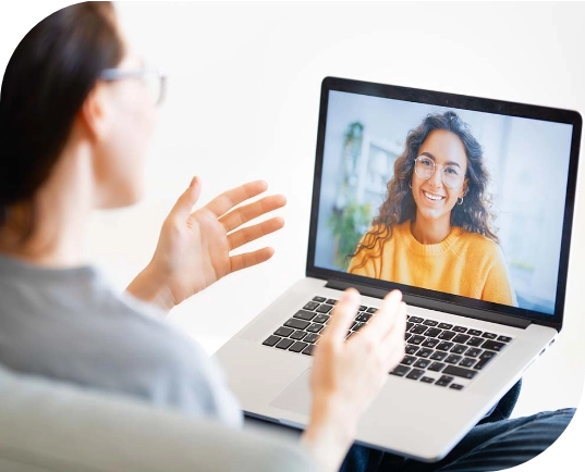 A person having an online coaching session, showing a smiling woman in a yellow sweater on her laptop screen