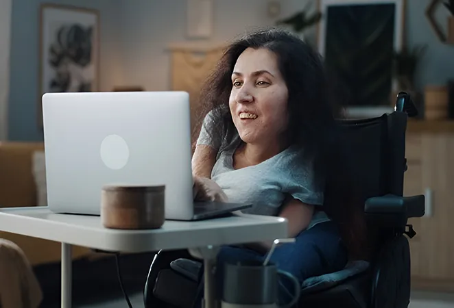 A woman with curly hair smiles while taking notes during ot session and looking at her laptop.