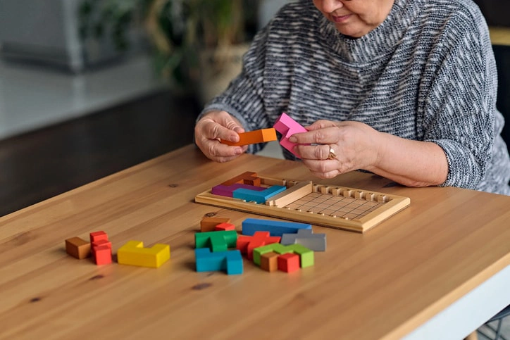 An elderly woman uses colourful blocks for an occupational therapy exercise at home, showcasing remote therapy benefits.