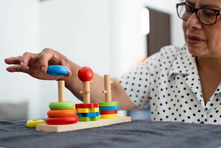 Woman practising fine motor skills with a colourful pegboard, showcasing an occupational therapy activity aimed at improving hand coordination.