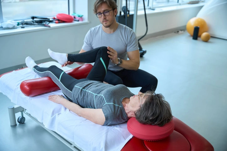 Physiotherapist helping a senior woman with leg exercises during a physical rehabilitation session to improve mobility and strength.