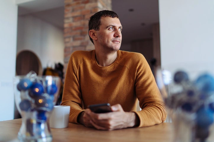 Man sitting at a table, deep in thought, reflecting on mental health, representing occupational therapy's role in adult well-being.