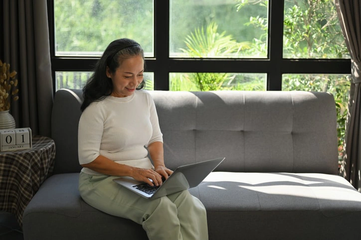 Woman sitting on a sofa with a laptop, researching is occupational therapy is covered by the NDIS.