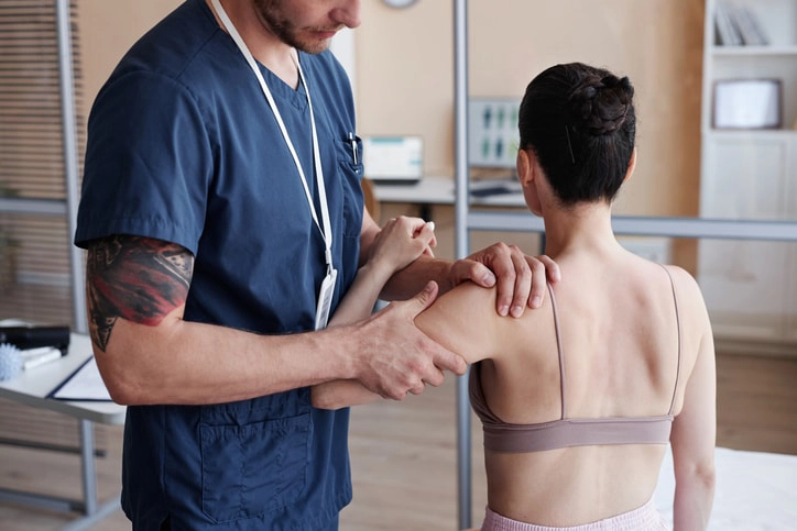 Physiotherapist conducting shoulder therapy with a female patient to enhance movement, strength, and physical function.