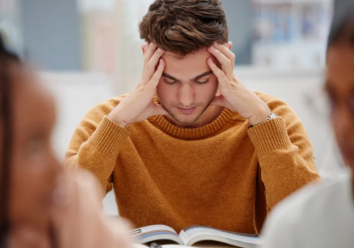 A young man with autism experiencing stress while studying, highlighting the challenges in emotional regulation and focus that occupational therapy can help address.