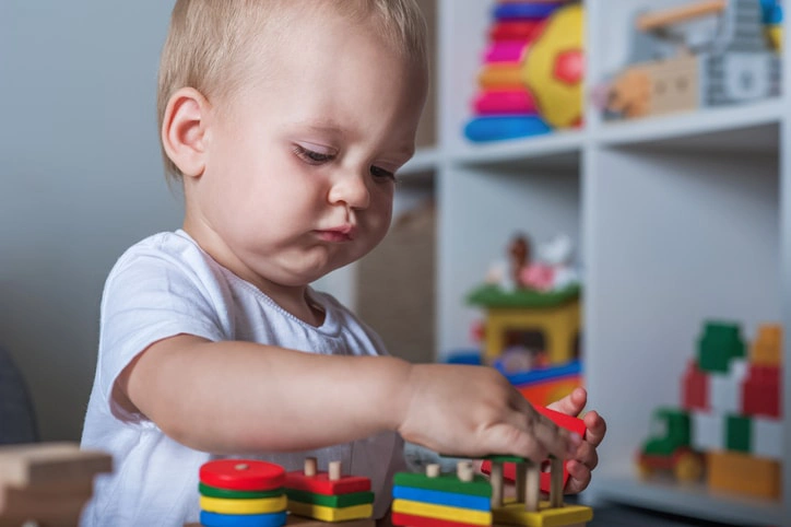 Toddler playing with stacking blocks, demonstrating early intervention through occupational therapy to develop motor skills.