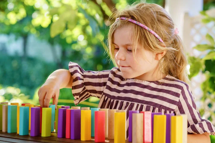 Child playing with colourful blocks outdoors working on her goal to improve motor skills