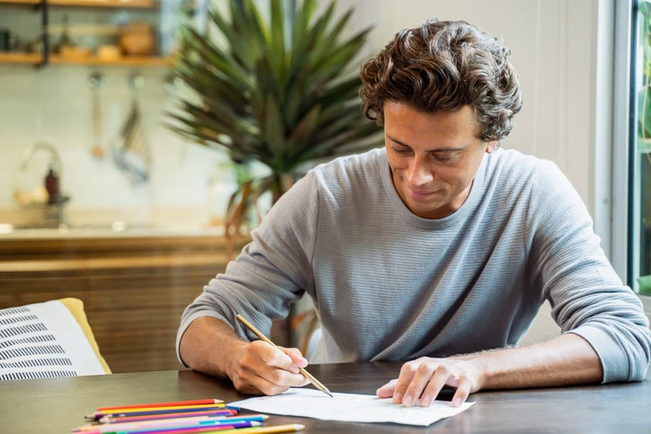 Young man writing notes at a desk, utilising planning and organisational strategies to manage ADHD symptoms."Enhancing Organisation and Planning.